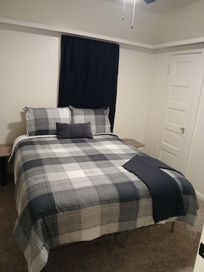 Quarto com cama, mesa de cabeceira, porta e luminária no teto.
