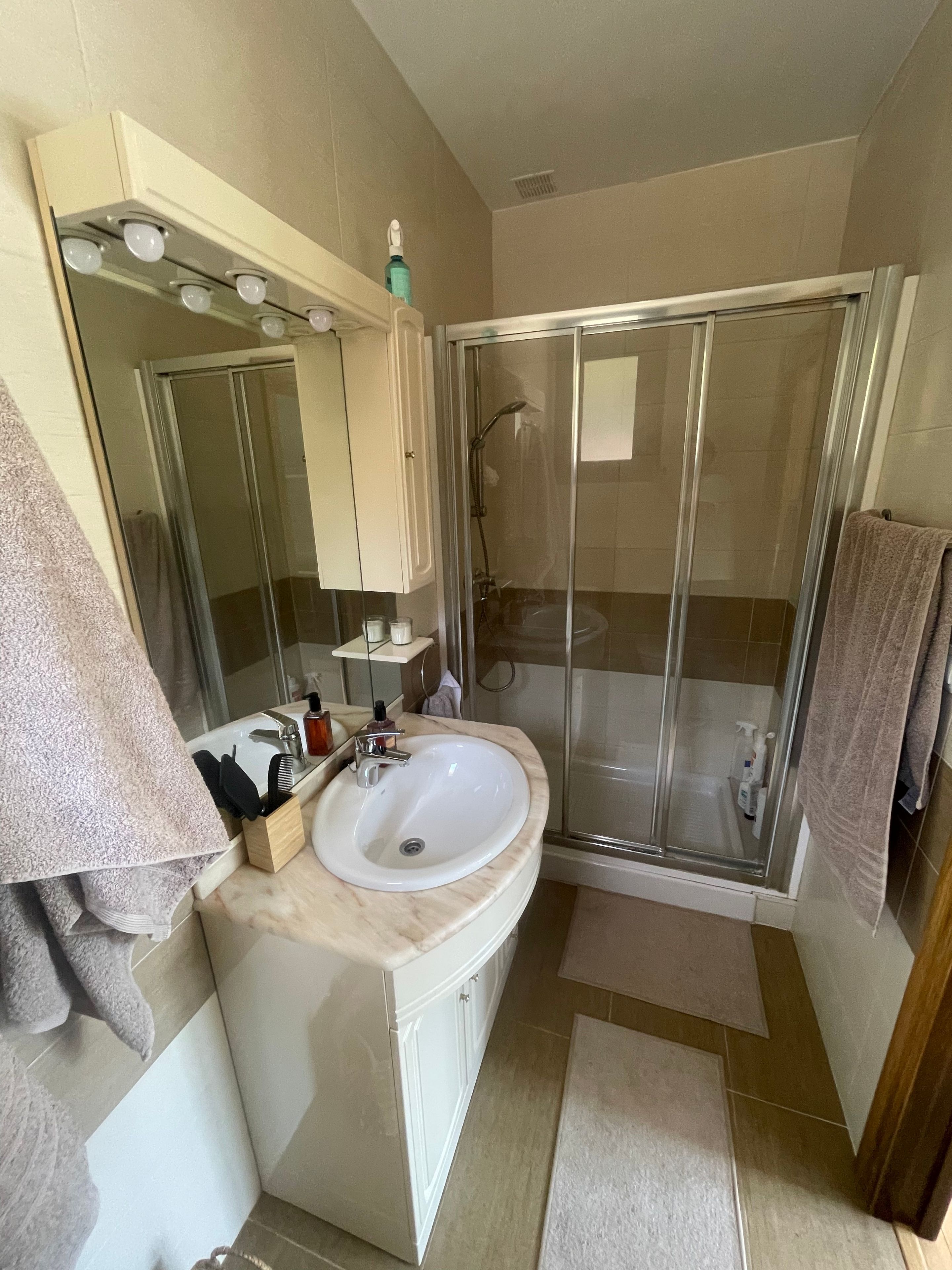 Un baño con un lavamanos blanco, un espejo, una cabina de ducha de cristal y un perchero para toallas.