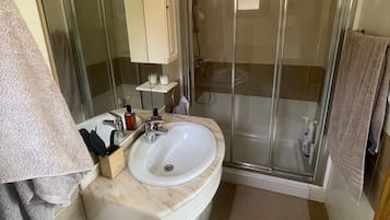 Un baño con un lavamanos blanco, un espejo, una cabina de ducha de cristal y un perchero para toallas.