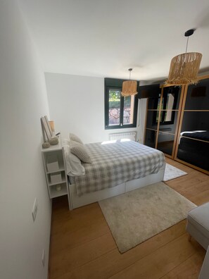 Un dormitorio con cama, ventana, radiador, armario y una lámpara colgante.