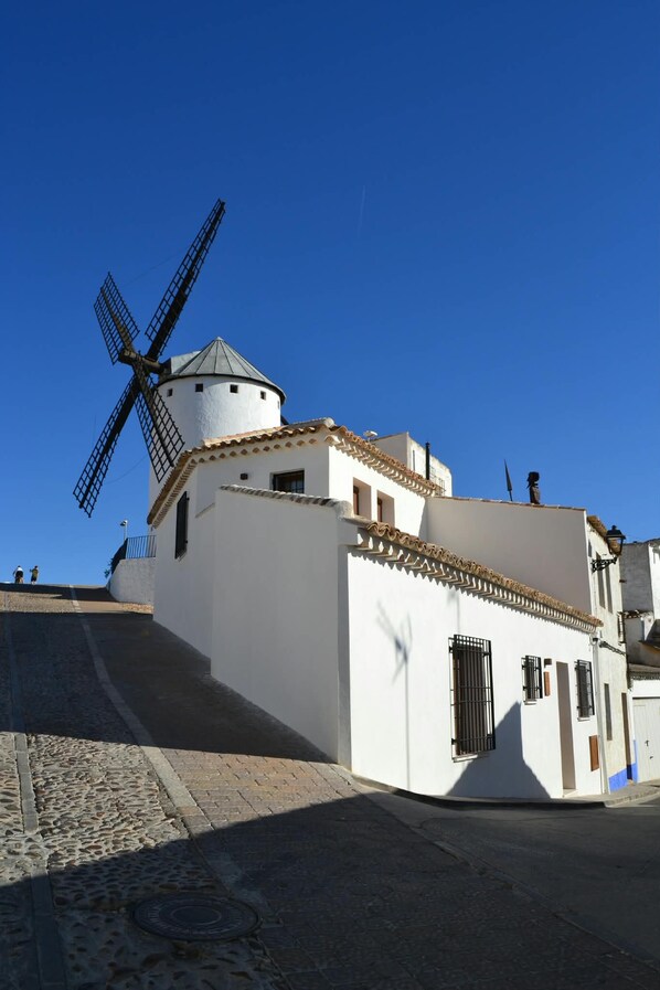 A traditional windmill attached to a white building with a tiled roof and a small tower. - New Listing (Campo de Criptana)