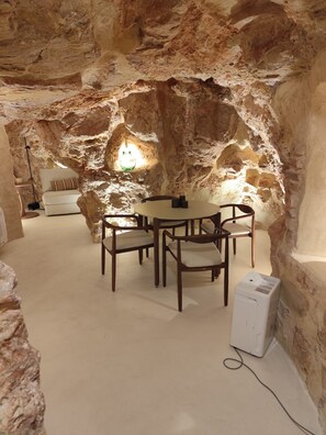 A dining area with a round table and chairs, a sofa, and a hanging light fixture in a cave-like interior. - New Listing (Campo de Criptana)