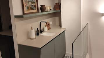 Un baño con un lavamanos moderno, un espejo y una repisa con objetos decorativos.