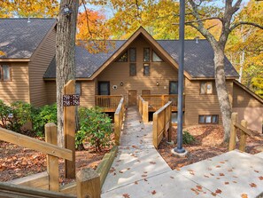 A wooden lodge with a central staircase leading to a porch, surrounded by trees with autumn leaves. - Heart of Wintergreen 1BR - Fully Stocked, Year-Round, Couples & Families (Wintergreen Resort)
