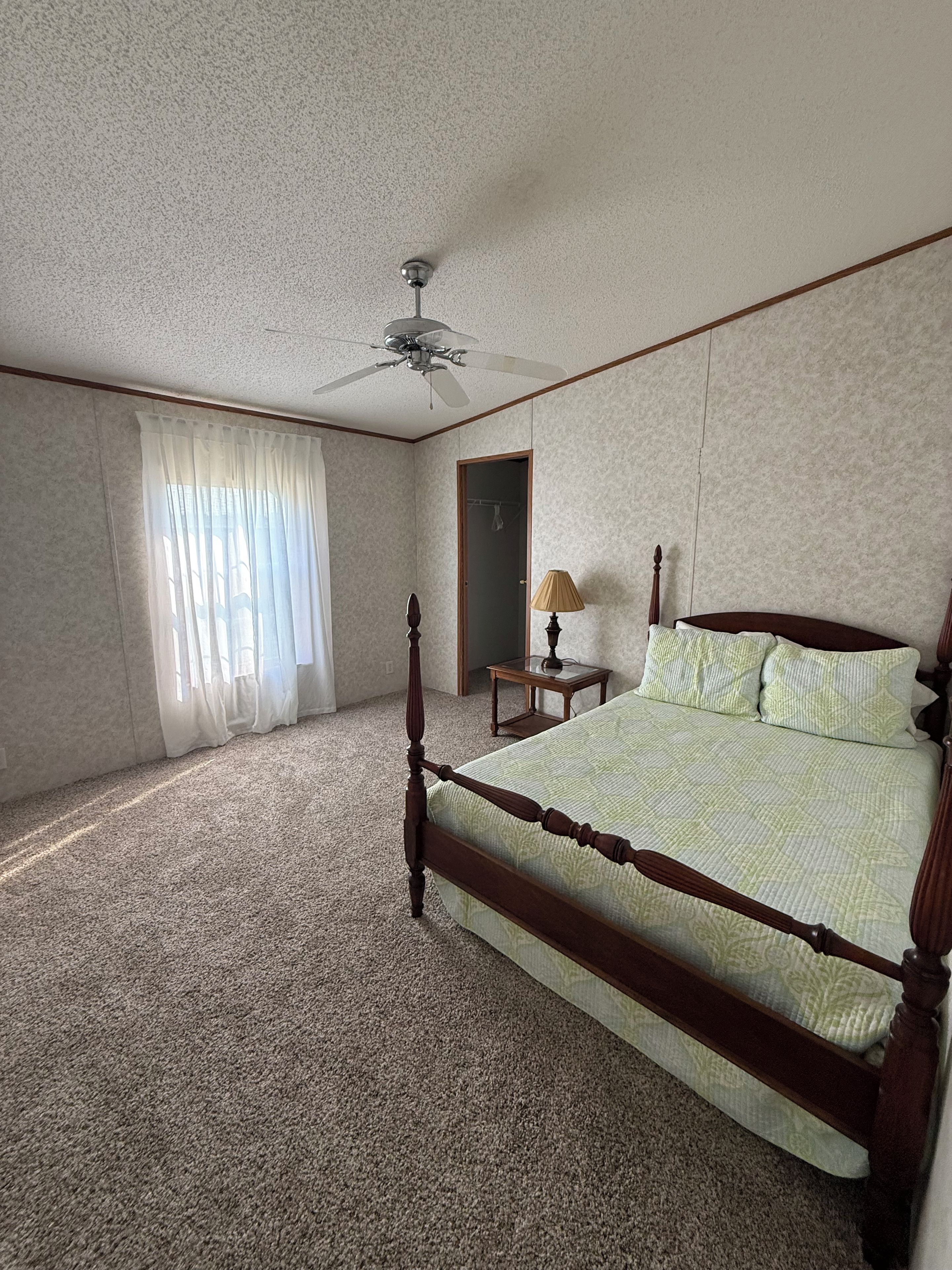 Un dormitorio con una cama con dosel, un ventilador de techo, una mesita de noche y una lámpara.