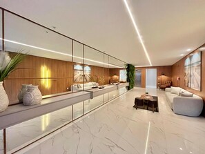 Un intérieur moderne avec une longue cloison en verre, un espace salon comprenant un canapé et des fauteuils, et un sol en marbre.