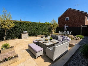 Une terrasse avec des meubles d’extérieur, un barbecue et une maison en briques en arrière-plan.