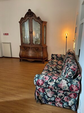 Ein Zimmer mit Holzboden, einem floralen Sofa und einer großen Holzkommode mit Glastüren.