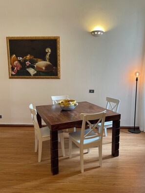 Ein Essbereich mit einem Holztisch, weißen Stühlen, einem Bild an der Wand und einer Stehlampe.
