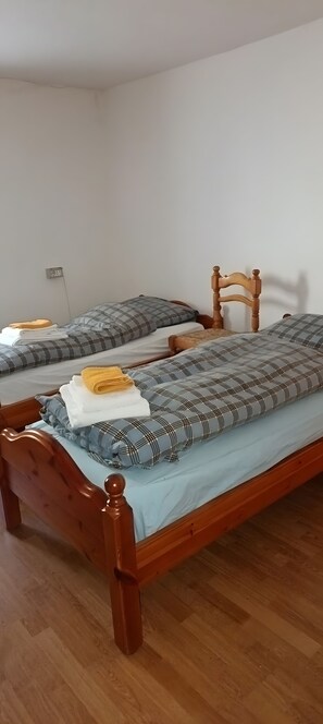 Dos camas de madera con estructuras metálicas, ropa de cama gris y blanca, y una silla de madera.
