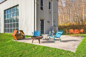 A modern building with large windows, a patio with outdoor furniture, and a fire pit. - The Looking Glass Modern Vermont Retreat with Private Hot Tub (Barnard)