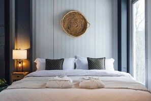 A hotel room with a bed, pillows, a bedside lamp, a woven wall hanging, and a window. - The Looking Glass Modern Vermont Retreat with Private Hot Tub (Barnard)
