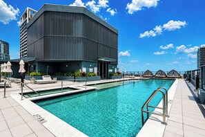 En moderne bygning med et poolområde, der inkluderer en swimmingpool, liggestole og parasoller.