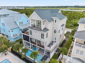 A multi-story house with a pool, surrounded by greenery and other houses. - Luxury Coastal Estate + Ocean & ICW View + Private Pool + Grand Piano & Wine Bar (Ocean Isle Beach)