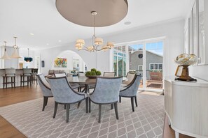 A dining area with a round table, six chairs, and a chandelier. - Luxury Coastal Estate + Ocean & ICW View + Private Pool + Grand Piano & Wine Bar (Ocean Isle Beach)