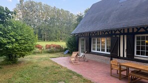 Ein Gebäude mit dunklem Dach, weißen Fensterrahmen und einer Ziegel-Fassade, mit einer Terrasse, die einen Tisch und Stühle bietet.