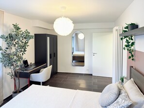 Une chambre à coucher moderne, comprenant un lit, un bureau, une chaise, une armoire et un luminaire suspendu.