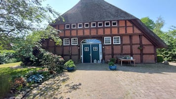 Een traditioneel vakwerkhuis met een steil rieten dak, een centrale ingang met een blauwe deur en een gevel van baksteen.