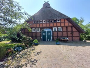 Een traditioneel vakwerkhuis met een steil rieten dak, een centrale ingang met een blauwe deur en een gevel van baksteen.