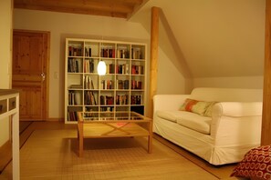 Een gezellige woonkamer met een witte bank, een houten salontafel en een boekenkast vol boeken.