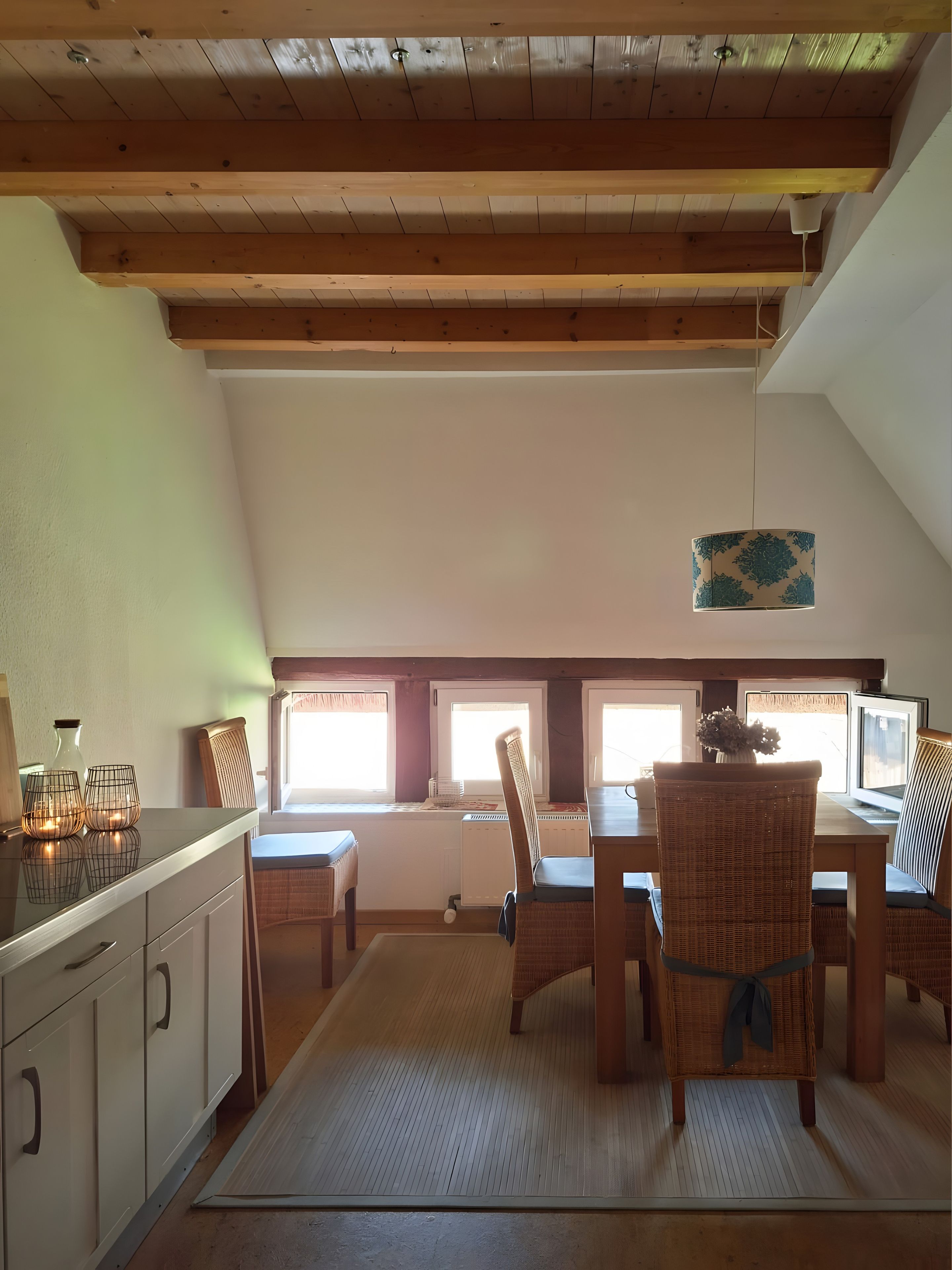 Een eetgedeelte met een hoge plafond, houten balken, een centrale tafel met stoelen en een uitzicht door ramen.