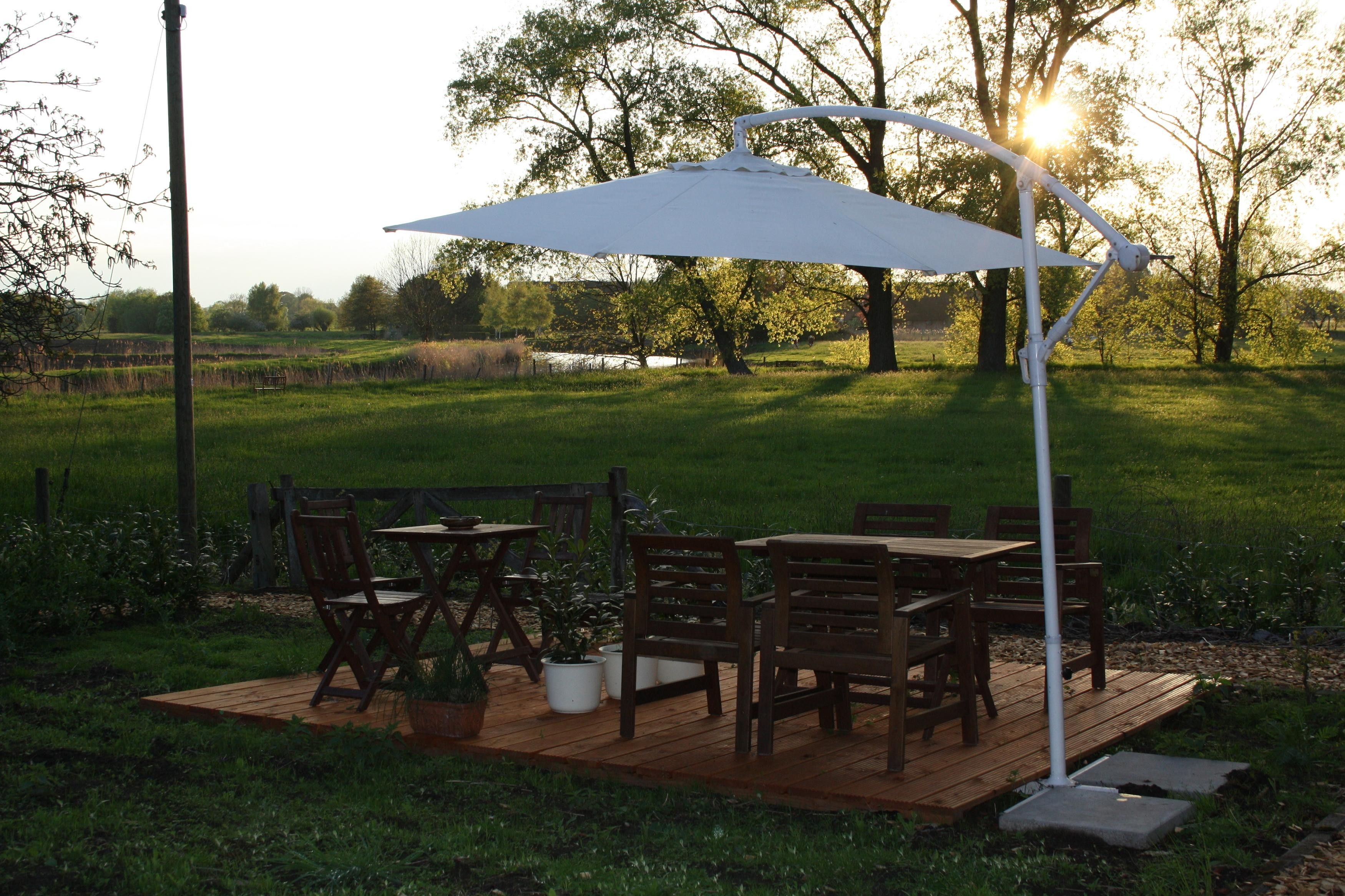 Een terras buiten, met een tafel en stoelen, omgeven door groen en bomen.
