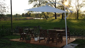 Een terras buiten, met een tafel en stoelen, omgeven door groen en bomen.