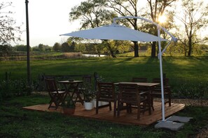 Um pátio externo com mesa e cadeiras, cercado por vegetação e árvores.