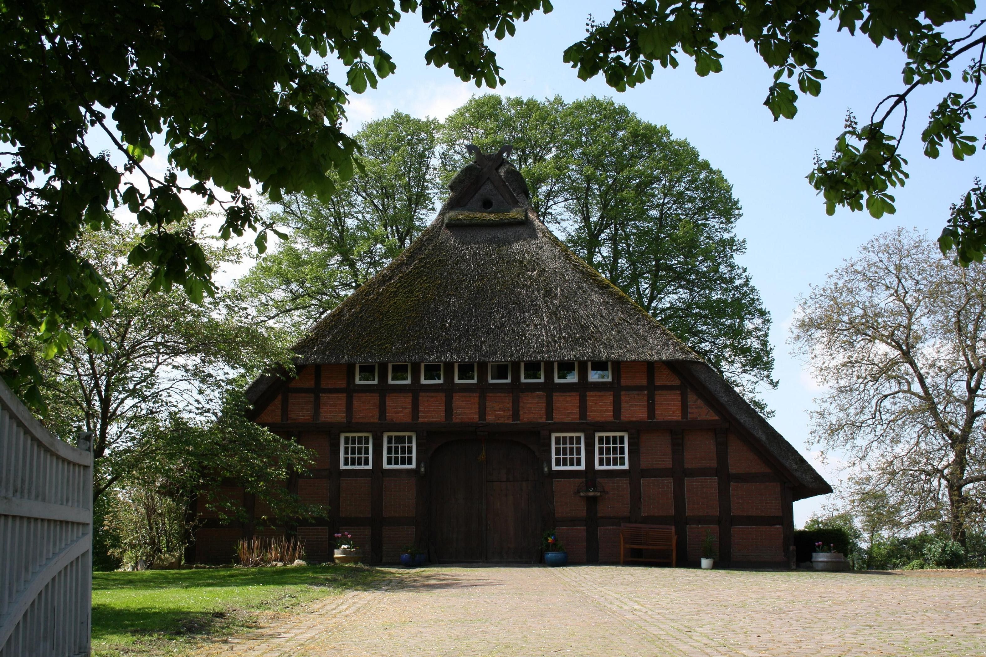 Een traditioneel gebouw met rieten dak, een grote houten deur en een bakstenen gevel.