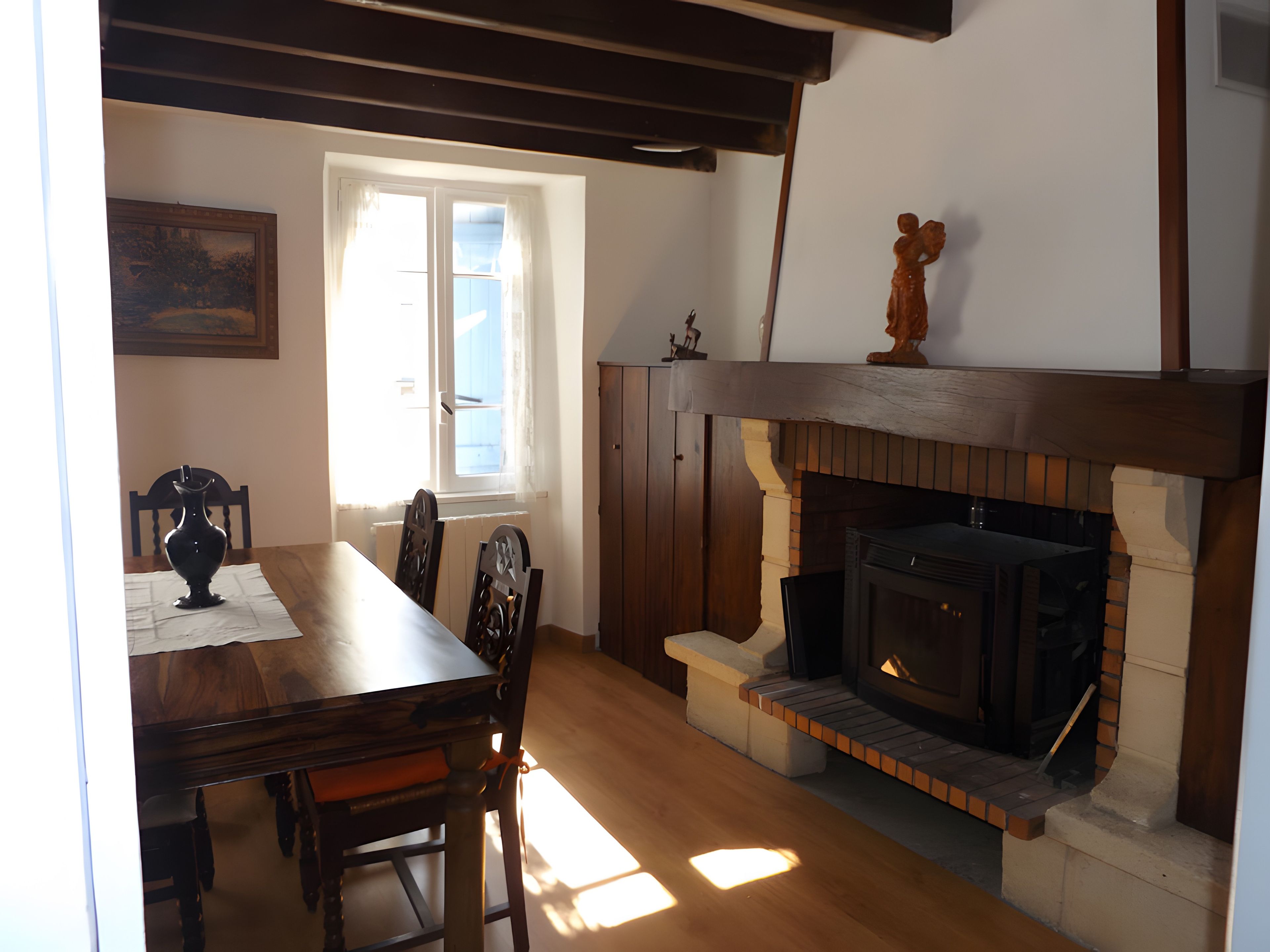 A dining area with a wooden table, chairs, a vase, and a fireplace.