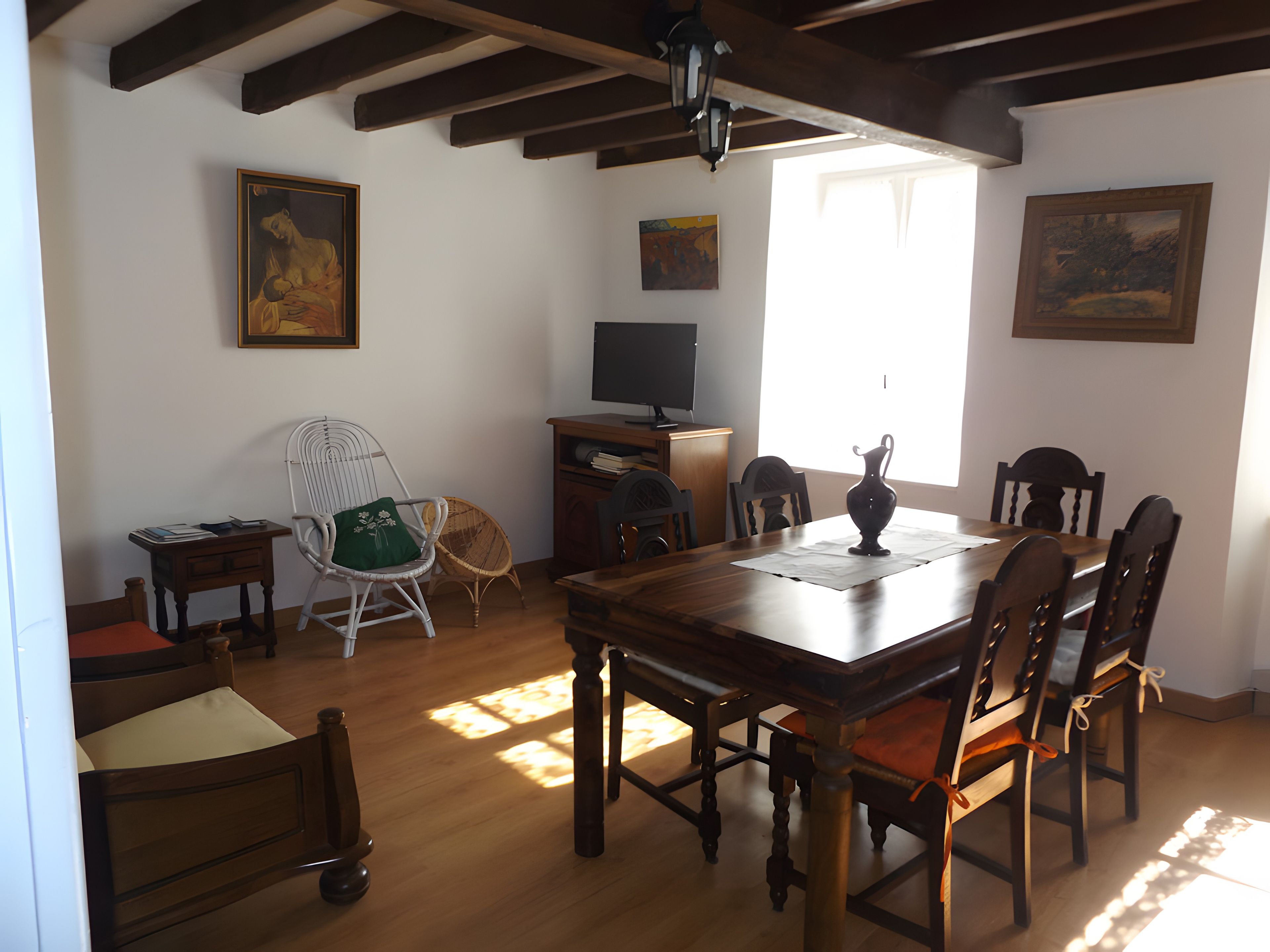 A dining area with a wooden table and chairs, a television, and artwork on the walls.