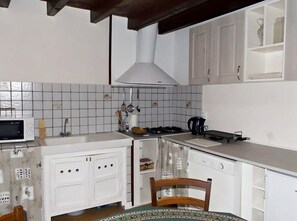 Een keuken met witte kastjes, een magnetron, een fornuis en een spoelbak.
