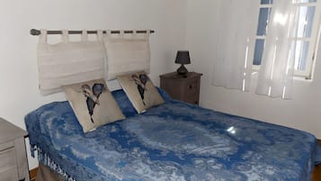 A bedroom with a bed, pillows, a nightstand, a lamp, and a window with curtains.