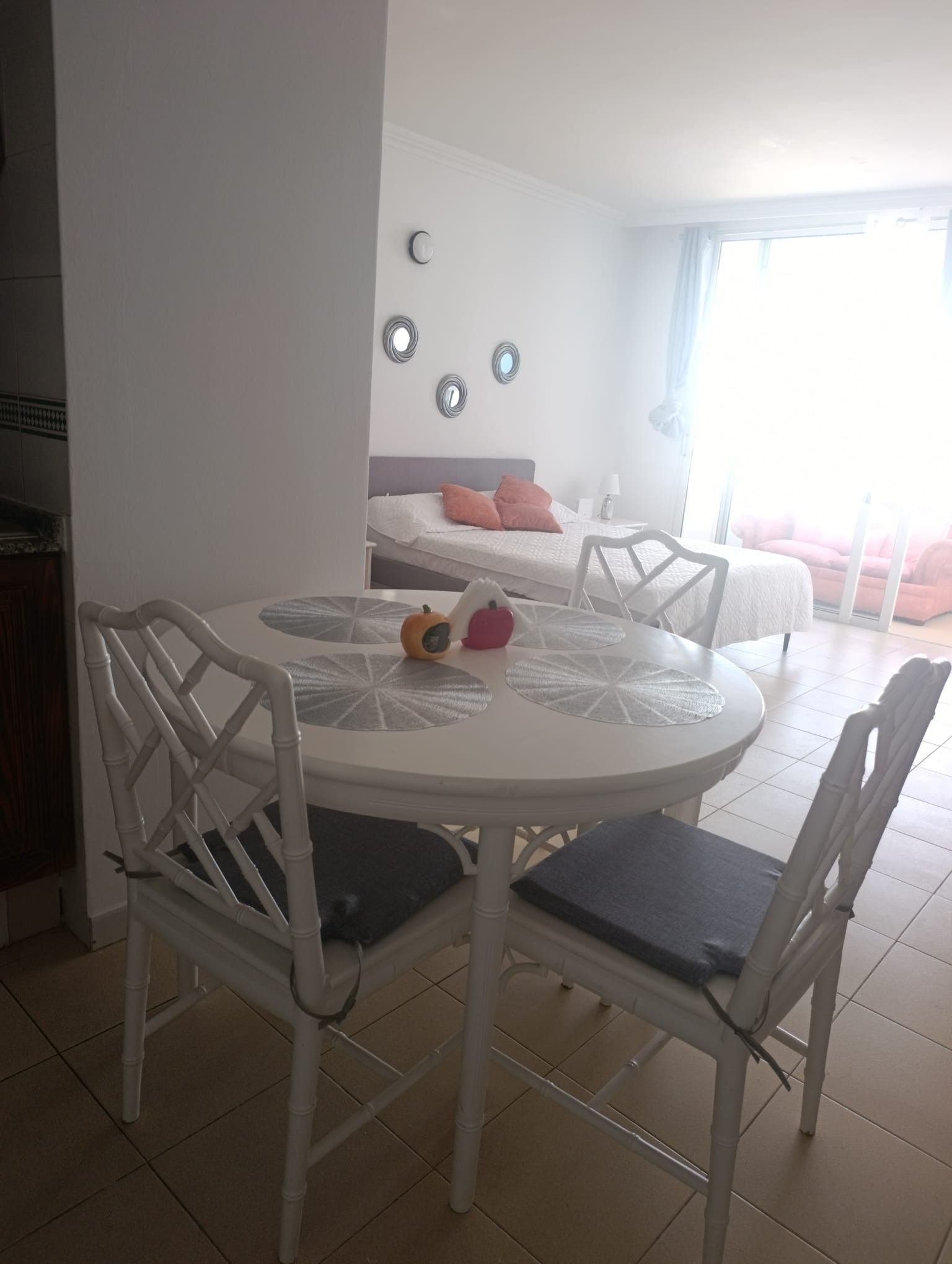 Een eetgedeelte met een ronde tafel en stoelen, een bed met kussens, en een raam met gordijnen.