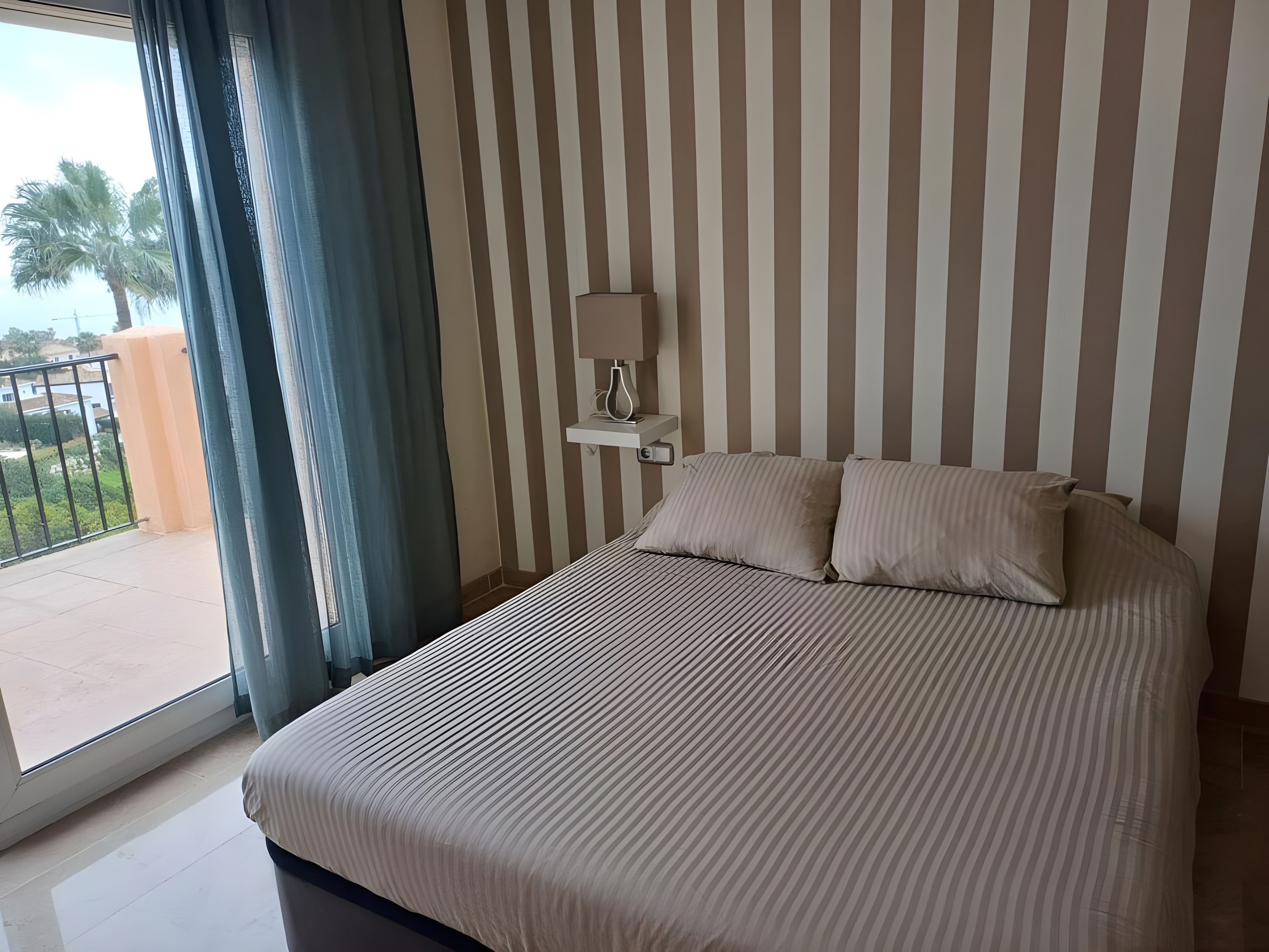 Une chambre d’hôtel avec un lit, une table de chevet, une lampe, une fenêtre avec des rideaux et une vue sur l’extérieur.