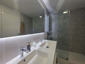 Ein modernes Badezimmer mit einem großen Spiegel, zwei Waschbecken und einer Duschkabine.