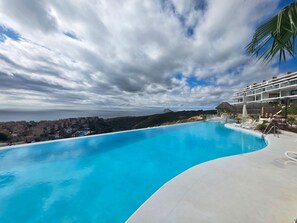 Ein geschwungener Infinity-Pool mit blauem Himmel und einem Berg im Hintergrund.