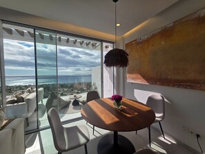 Ein moderner Essbereich mit einem runden Tisch, Stühlen und Meerblick durch große Fenster.