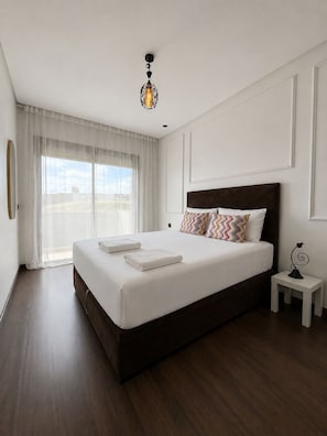 A hotel room with a large bed, a bedside table, a hanging light fixture, and a view through the window. - New Listing (Casablanca)