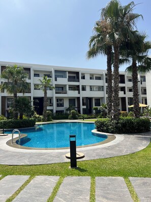 A modern building with a swimming pool surrounded by palm trees and a well-maintained lawn. - New Listing (Casablanca)