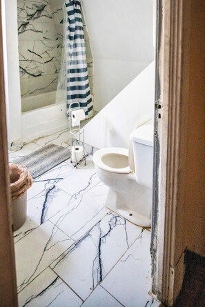 Un baño con inodoro, zona de ducha y suelo de mármol.