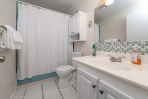 Casa de banho com sanita, cortina de chuveiro, lavatório com espelho e dispensador de sabonete.