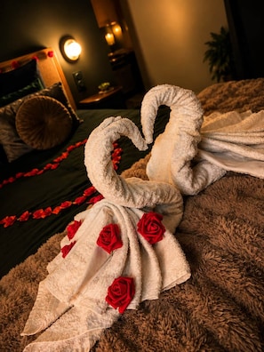 A bed with a towel arranged in the shape of a swan, adorned with red roses, and a red rose garland along the bed's edge. - Mana Suite & Spa - Luxury & Wellness (Tarare)