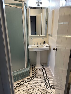Ein Badezimmer mit einem Standwaschbecken, einem Spiegel darüber und einem Fliesenboden mit sechseckigem Muster.