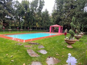 Ein rechteckiger Pool, umgeben von einer roten Umrandung, mit einer Laube im Hintergrund.