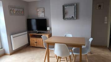 Een moderne woonkamer met een houten eettafel, witte stoelen, een flatscreen televisie en een radiator.
