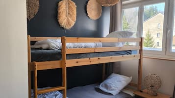Een stapelbed met houten frame, een nachtkastje met lamp en een raam met uitzicht op gebouwen.