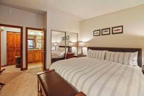 Una habitación de hotel con una cama grande, un banco de madera, un escritorio y un espejo.