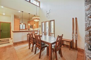 Comedor con mobiliario de madera, una lámpara de araña y una pared de piedra con esquíes.