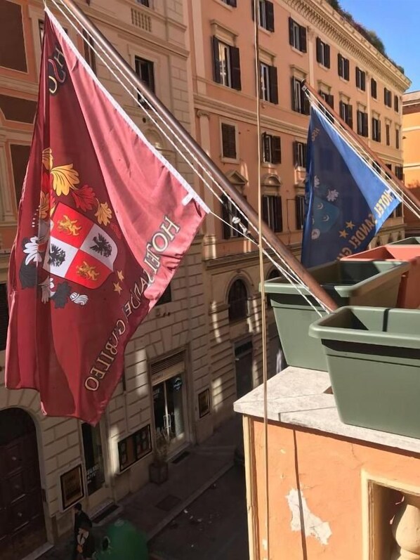 A building with multiple flags, including a red flag with a coat of arms and a blue flag with stars. - Sandel Giubileo Hotel (ROMA)